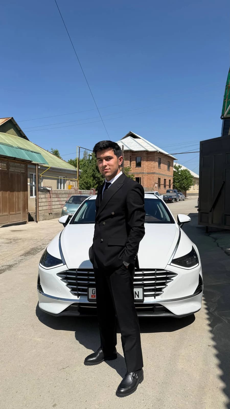 Halim in a black suit beside a white car